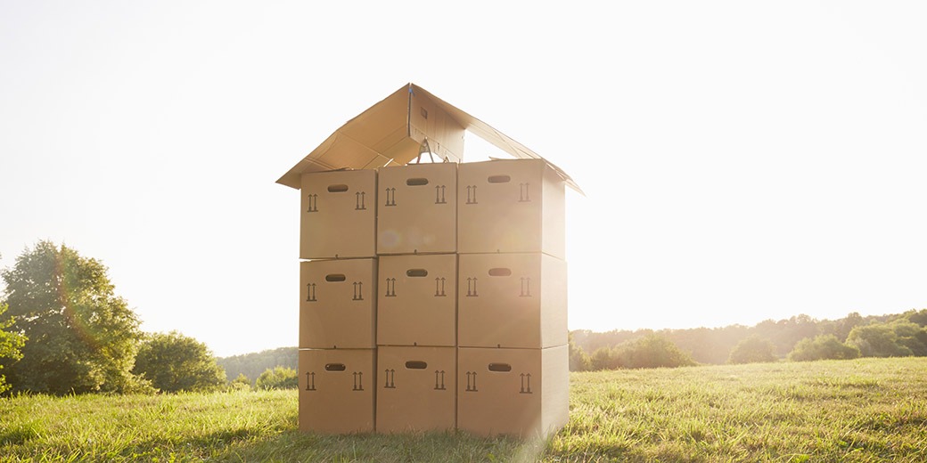 Stack of cardboard boxes on a meadow against sky, a house made of cardboard boxes